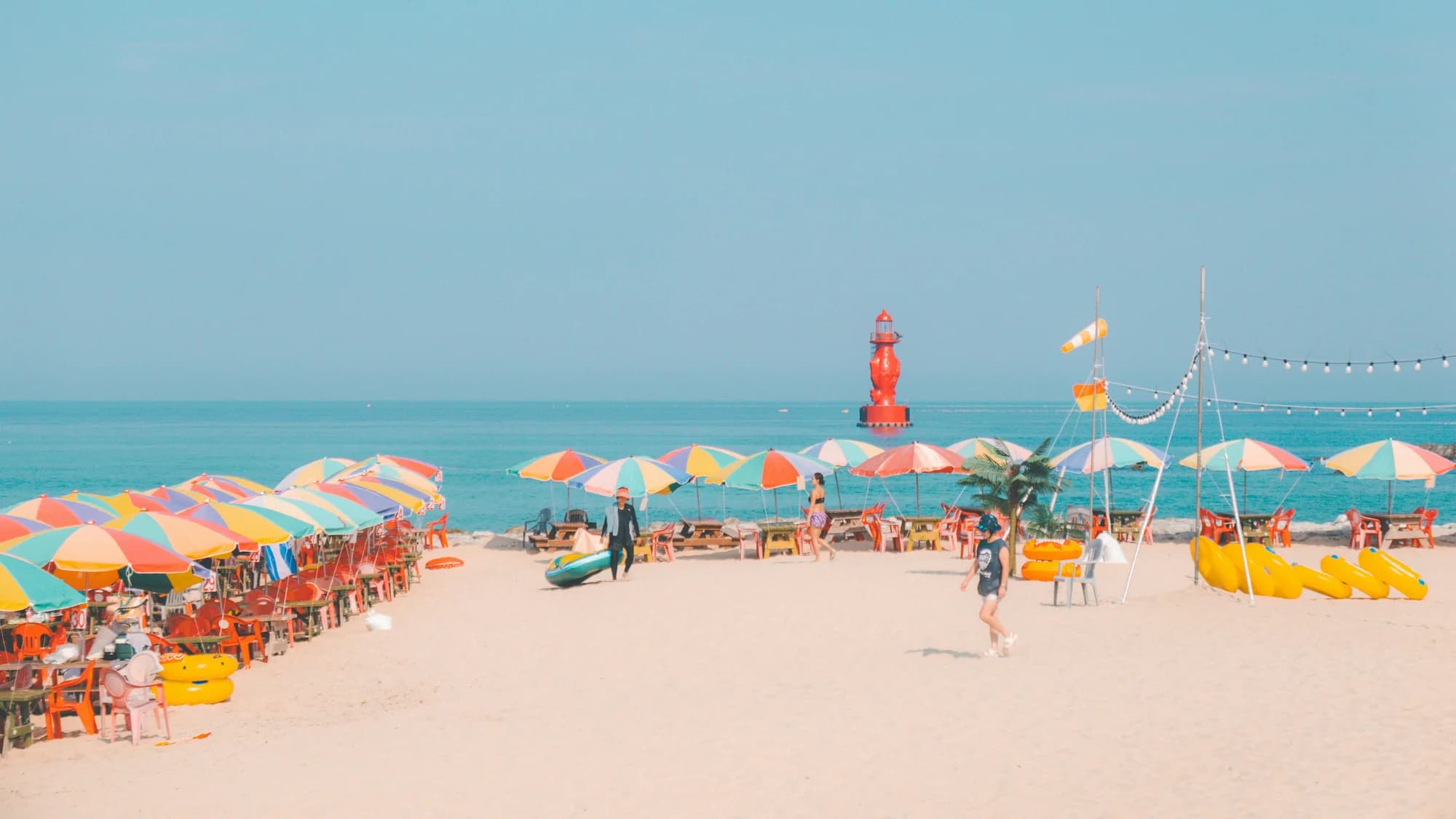 Colourful beach parasols beside the sea, with a red lighthouse offshore